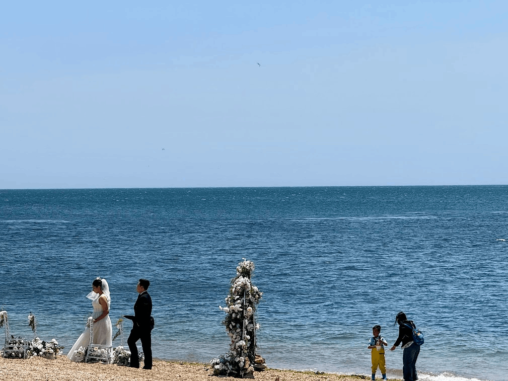 一对新婚夫妻正在拍婚纱照，花拱门背对着就是一个带娃的母亲